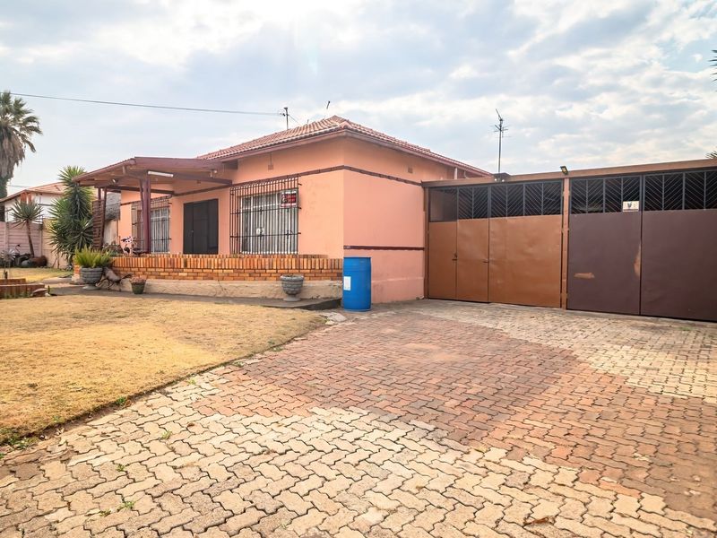 Front view of a single-story house featuring a brick driveway, secure metal gates, and a covered porch area with security bars on windows.