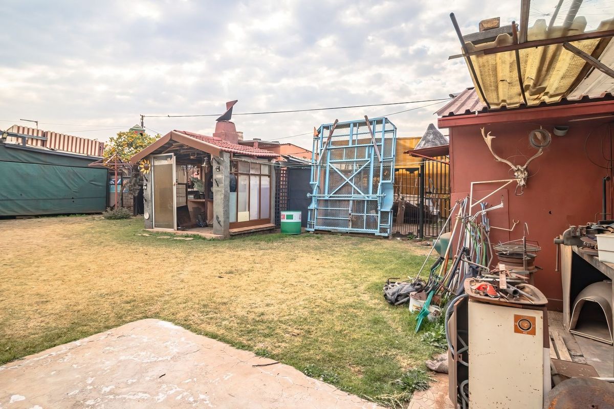 Rear garden area featuring a concrete patio, lawn, and a small outdoor structure with a fireplace, offering potential for landscaping and outdoor living improvements.