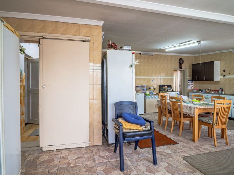 Open-plan kitchen and dining area featuring dated wall and floor tiling, built-in cabinetry, and fluorescent lighting, offering potential for modern renovation.