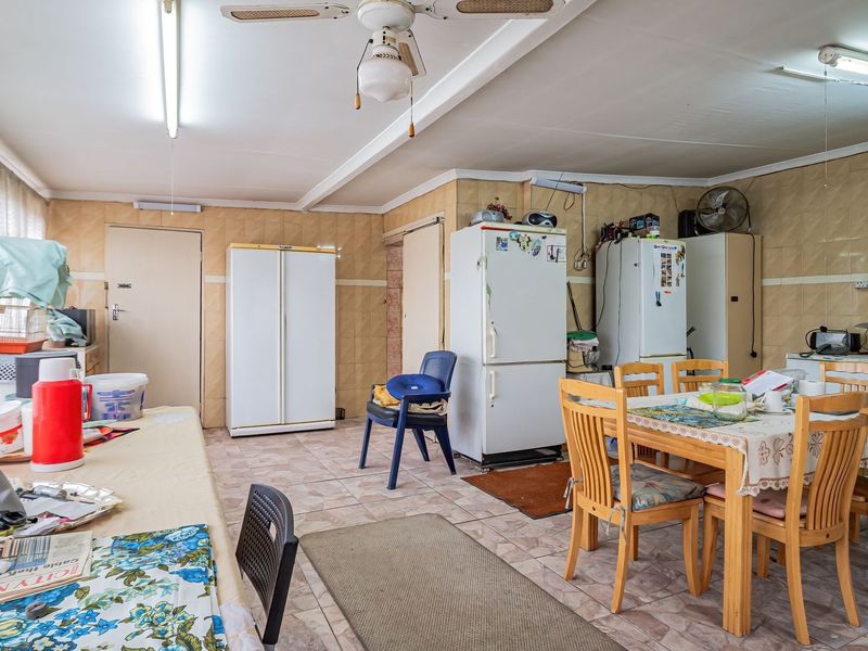 A spacious, dated kitchen area featuring tiled walls and flooring, equipped with a ceiling fan and fluorescent lighting, offering significant potential for modernization.