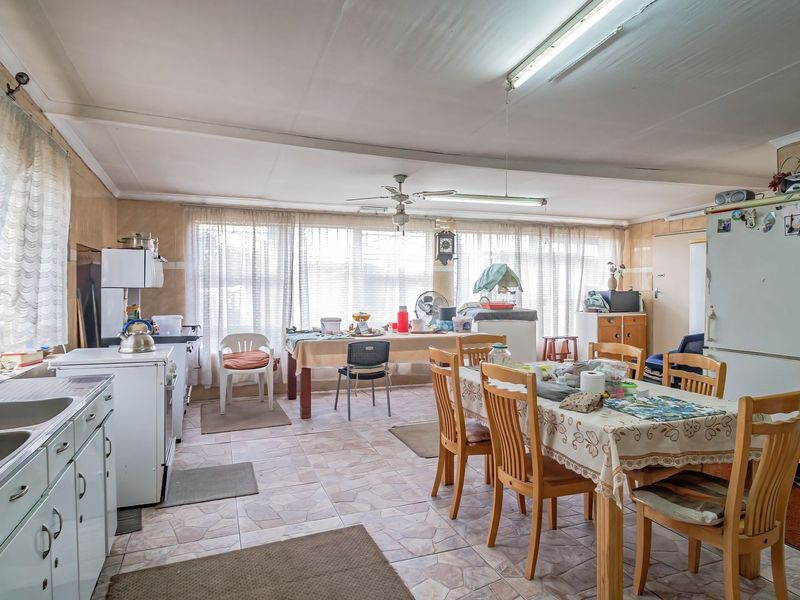 Spacious open-plan kitchen and dining area featuring tiled walls and flooring, offering a functional layout with potential for modern renovation.