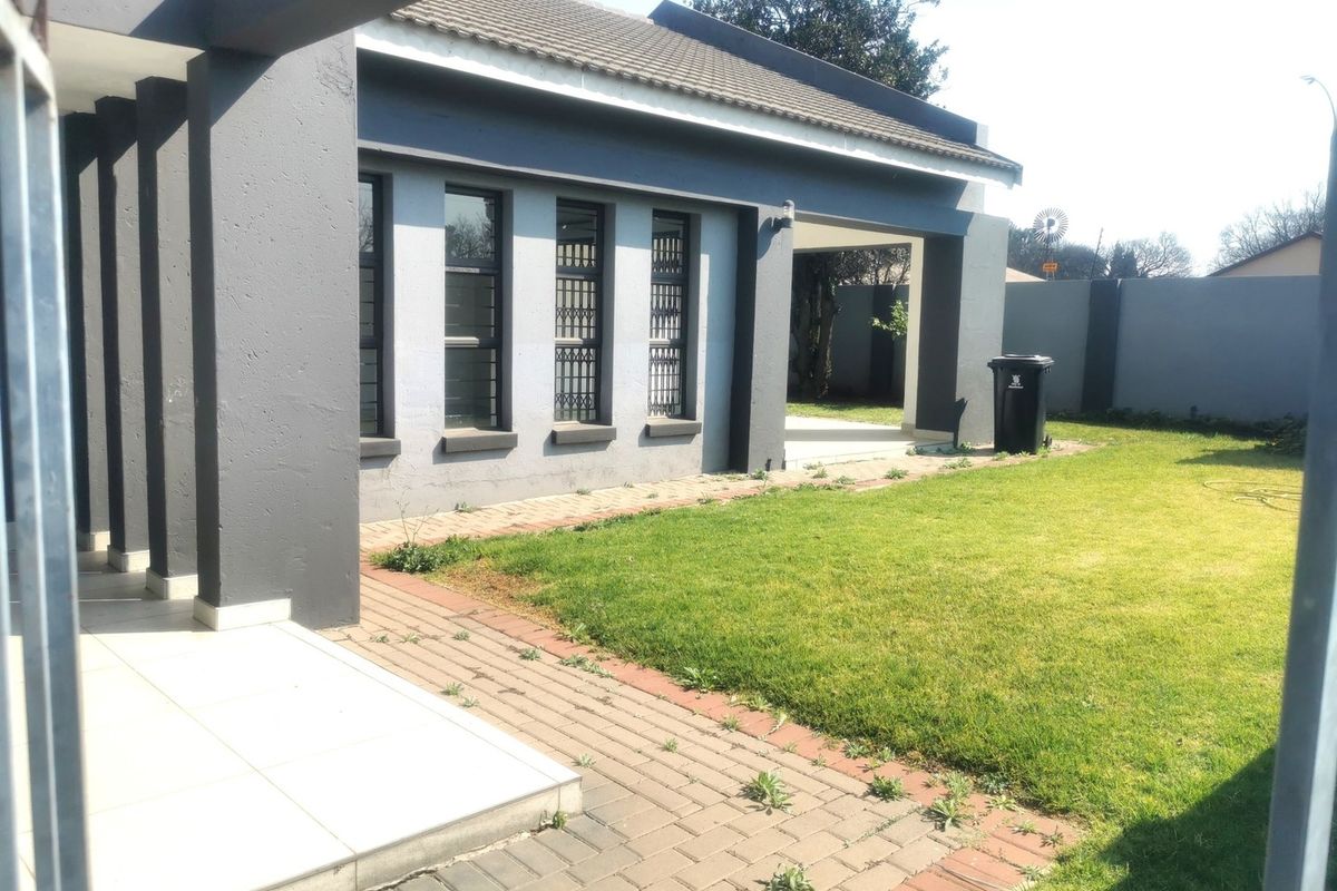 Rear exterior view of the house featuring a covered patio, paved walkway, and a well-maintained lawn enclosed by a perimeter wall.