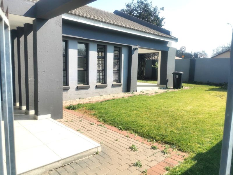Rear exterior view of the house featuring a covered patio, paved walkway, and a well-maintained lawn enclosed by a perimeter wall.