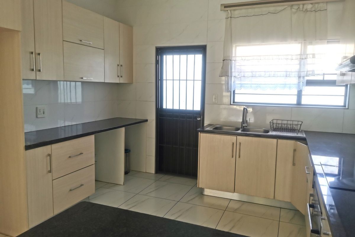 A clean, functional kitchen featuring light wood-finish cabinetry, dark countertops, tiled flooring, and a security door leading to the exterior.