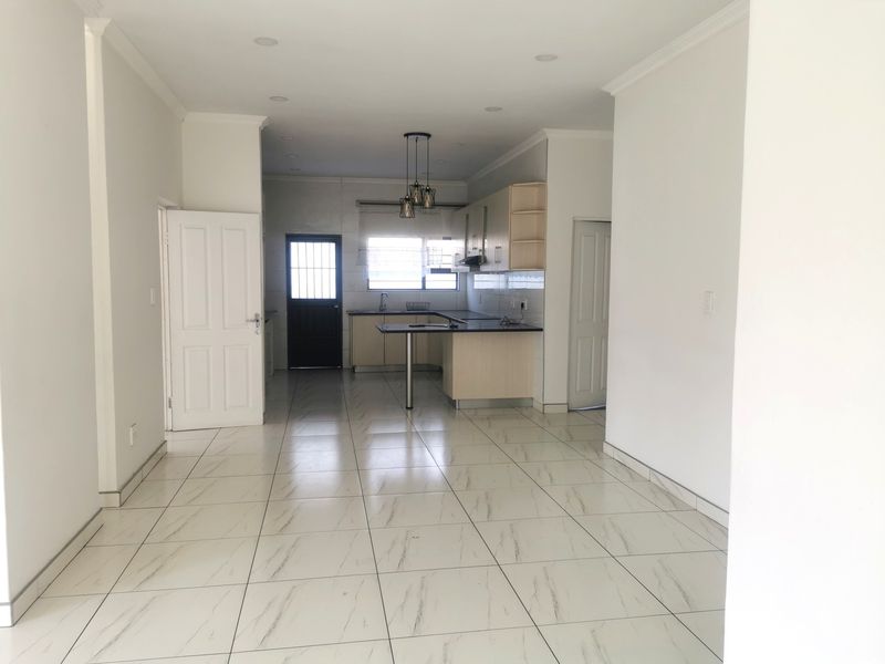 An open-plan living and kitchen area featuring modern tiled flooring, neutral walls, and a functional kitchen layout with built-in cabinetry and a breakfast bar.