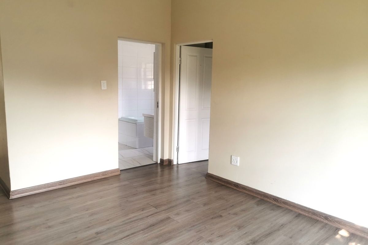 An empty bedroom featuring modern laminate flooring, neutral wall paint, and direct access to an adjoining bathroom.