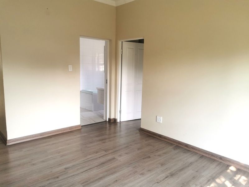 An empty bedroom featuring modern laminate flooring, neutral wall paint, and direct access to an adjoining bathroom.