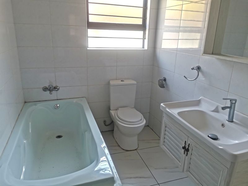 A functional bathroom featuring a bathtub, toilet, and vanity basin with tiled walls and flooring throughout.