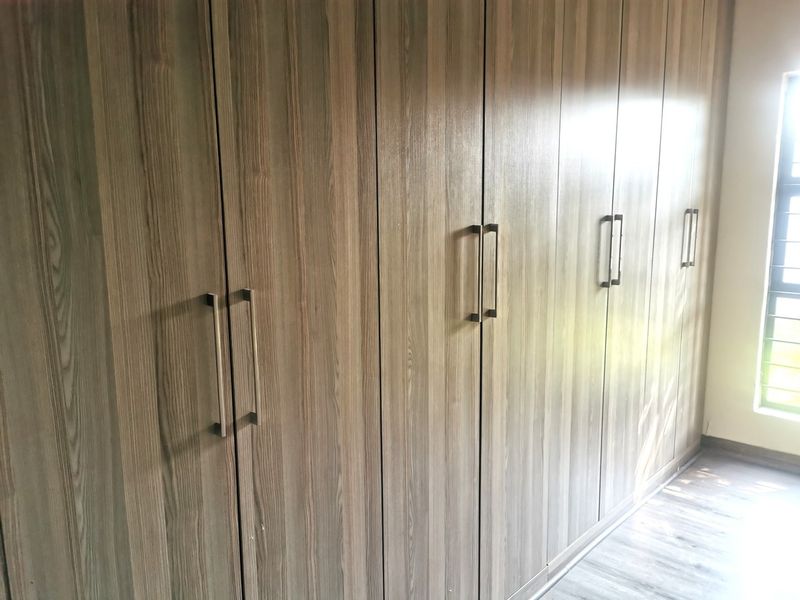 A bedroom featuring extensive floor-to-ceiling built-in cupboards with modern wood-grain finish and durable laminate flooring.