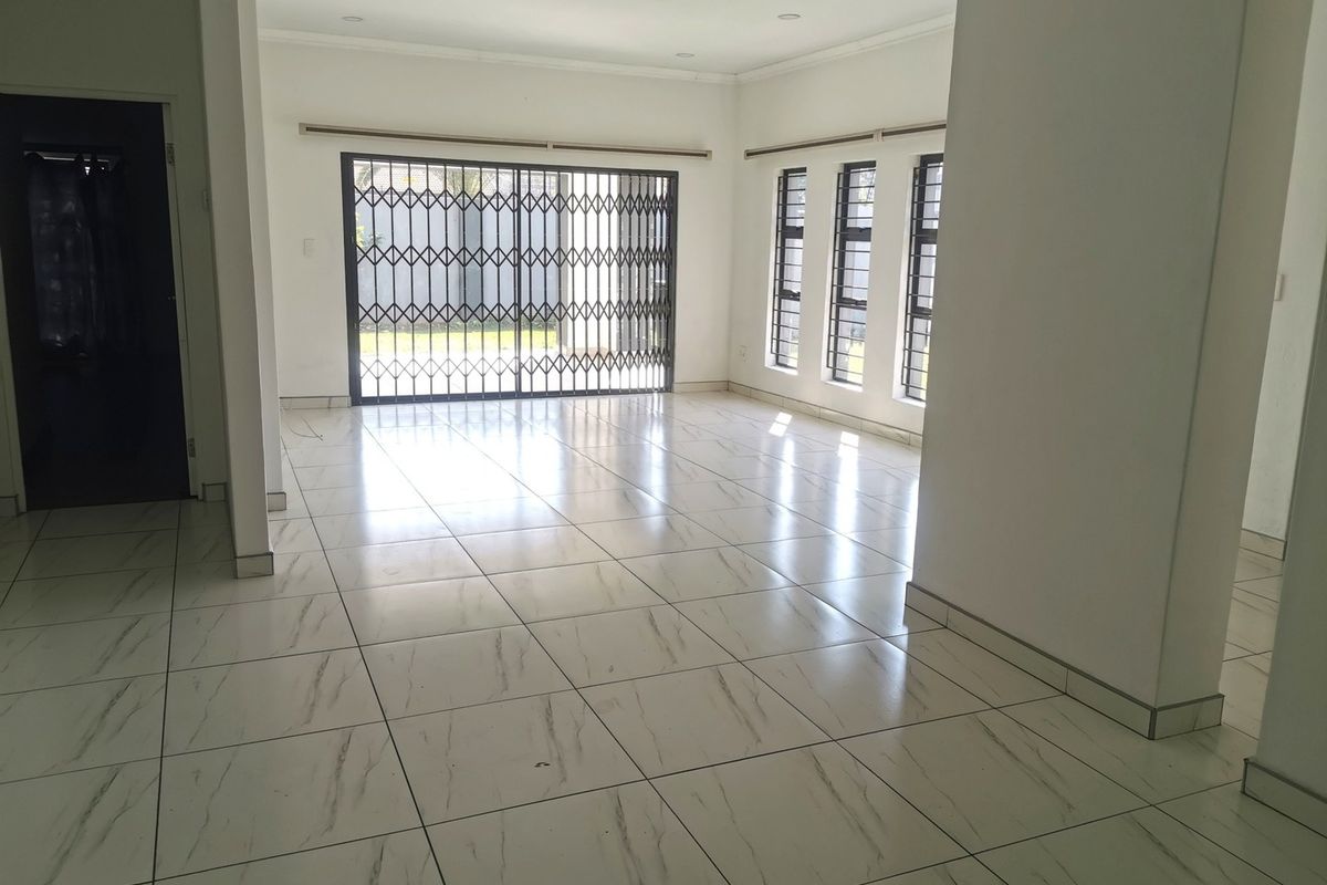 A bright, open-plan living area featuring modern marble-look floor tiles, recessed lighting, and large windows with security bars leading to the exterior.