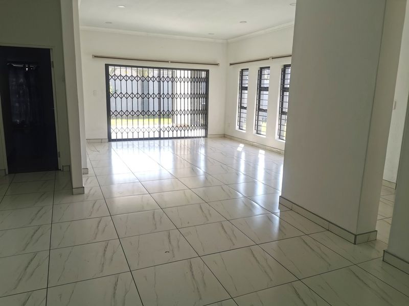 A bright, open-plan living area featuring modern marble-look floor tiles, recessed lighting, and large windows with security bars leading to the exterior.