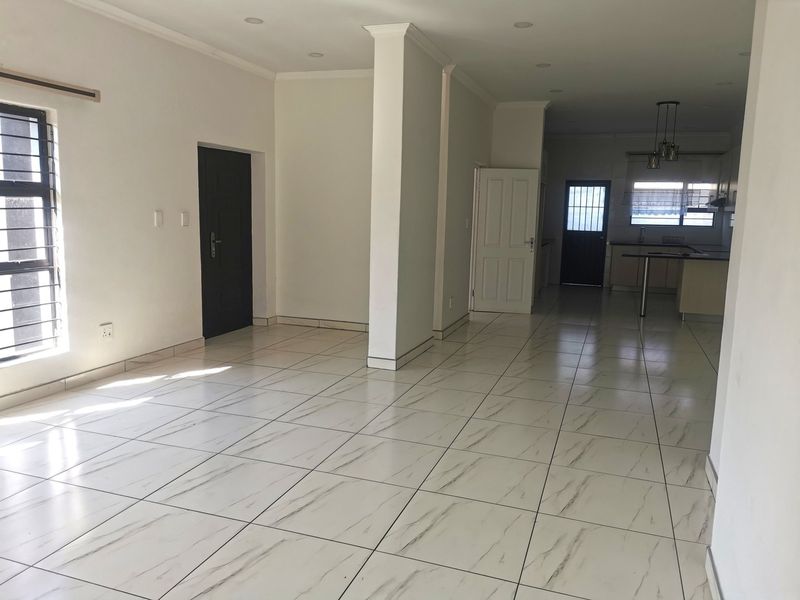 Spacious open-plan living area featuring modern tiled flooring, recessed lighting, and a connected kitchen space with built-in cabinetry.