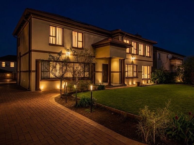 A well-maintained double-story residential property at dusk, featuring a paved driveway, manicured lawn, and integrated exterior lighting.