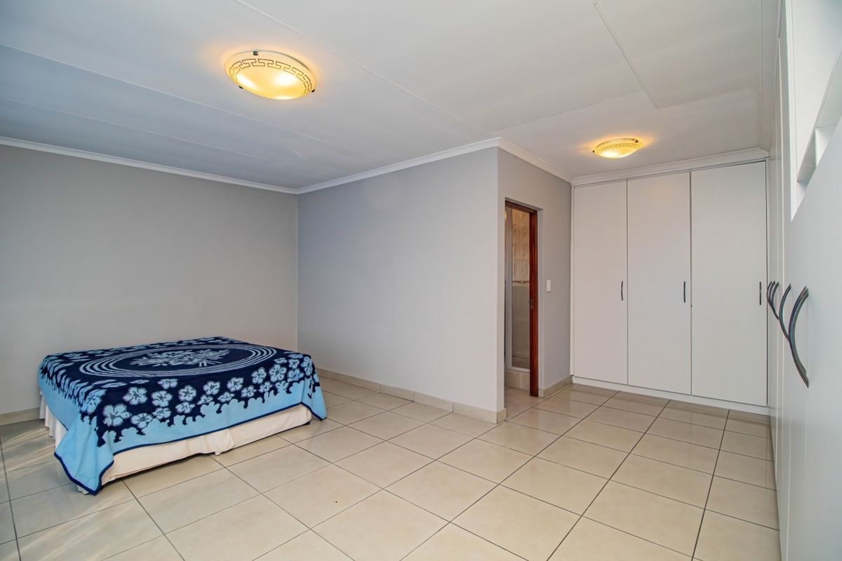 A spacious bedroom featuring neutral tiled flooring, built-in cupboards, and direct access to an en-suite bathroom.
