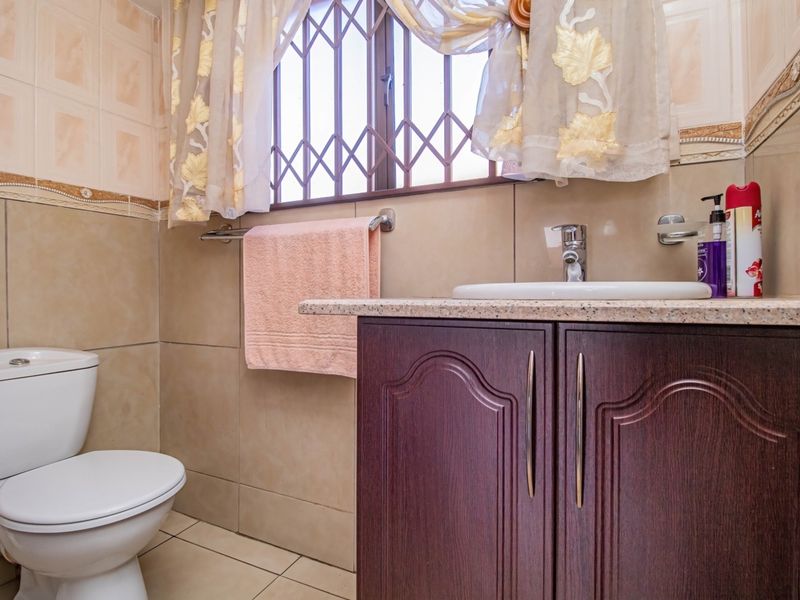 A functional bathroom featuring a vanity cabinet with a granite countertop, ceramic basin, and a standard toilet, finished with neutral wall and floor tiles.