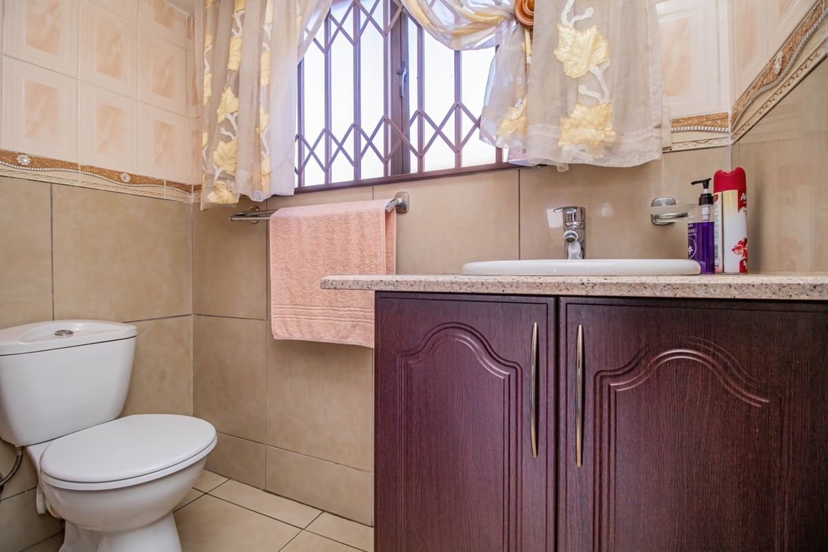 A functional bathroom featuring a vanity cabinet with a granite countertop, ceramic basin, and a standard toilet, finished with neutral wall and floor tiles.