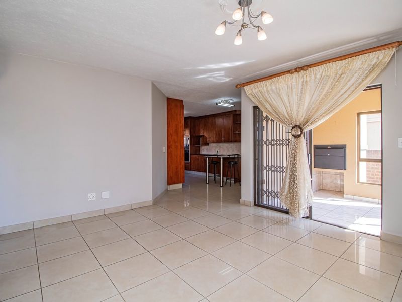 Open-plan living area featuring tiled floors, flowing into a kitchen with wooden cabinetry and leading out to a covered patio with a built-in braai.