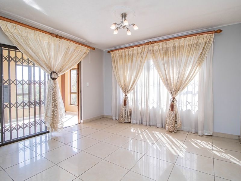 A bright and spacious living area featuring neutral tiled flooring, large windows with natural light, and direct access to an outdoor patio area.