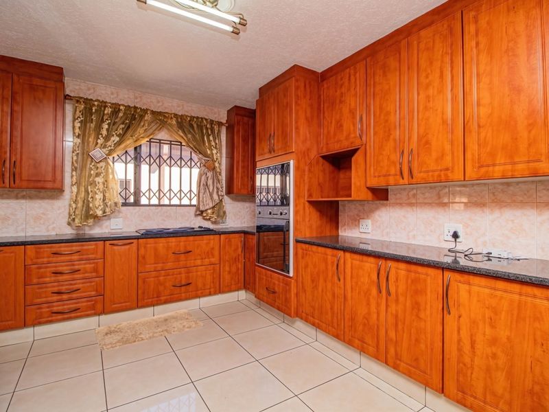 A functional kitchen featuring warm-toned wooden cabinetry, granite countertops, built-in oven, and tiled flooring with a window protected by security bars.