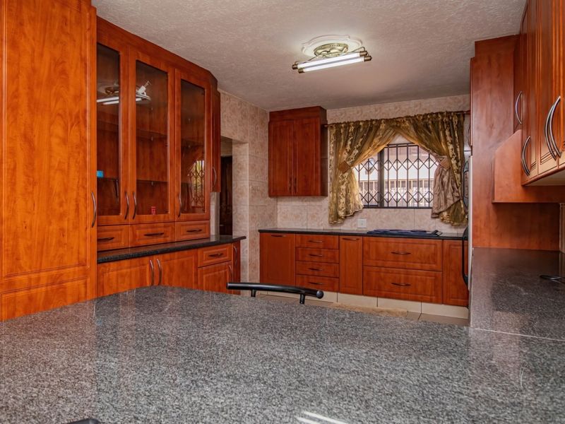 A functional kitchen featuring extensive wooden cabinetry, granite countertops, and tiled backsplash, offering ample storage and workspace.