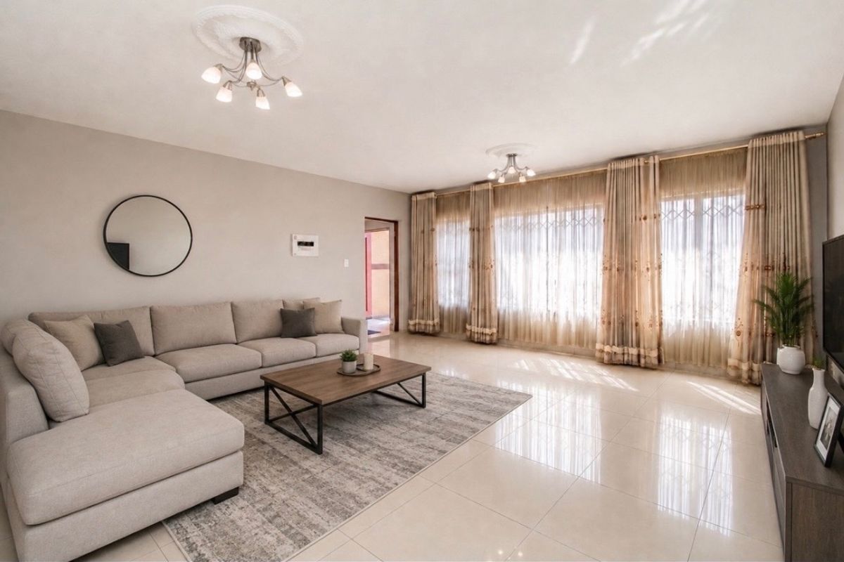 Spacious living room featuring polished tiled flooring, decorative ceiling roses, and large windows with natural light.