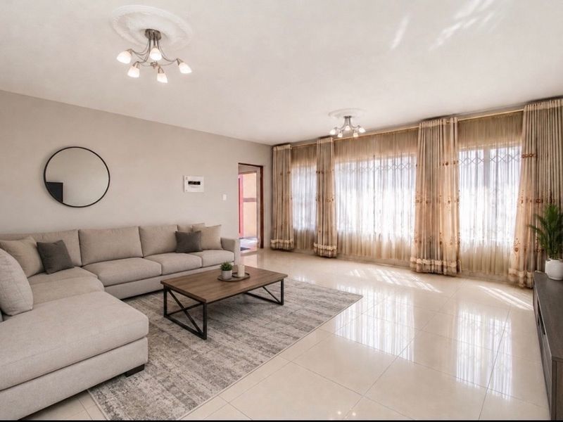 Spacious living room featuring polished tiled flooring, decorative ceiling roses, and large windows with natural light.