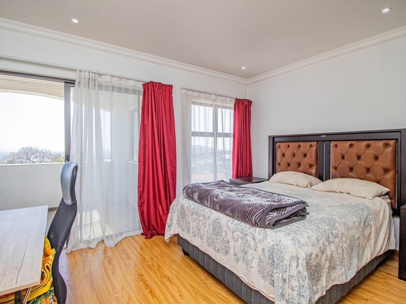 A well-lit bedroom featuring laminate flooring, recessed ceiling lights, and a sliding glass door providing access to an outdoor balcony.