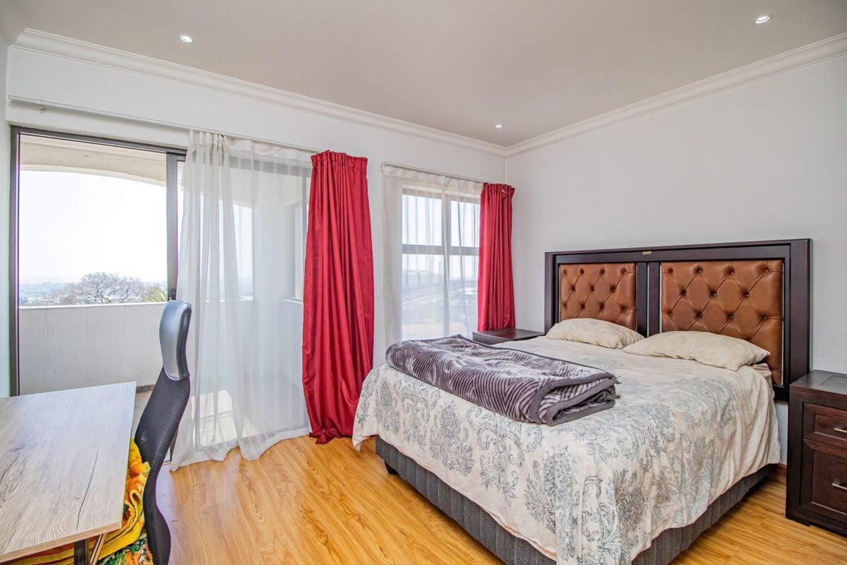 A well-lit bedroom featuring laminate flooring, recessed ceiling lights, and a sliding glass door providing access to an outdoor balcony.