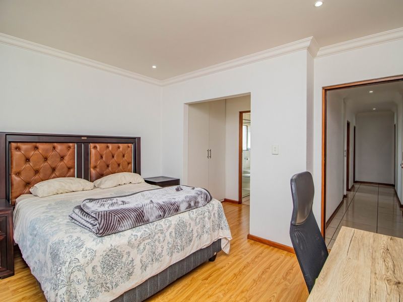 Spacious bedroom featuring laminate flooring, built-in cupboards, and recessed downlighting, with direct access to an en-suite bathroom and hallway.