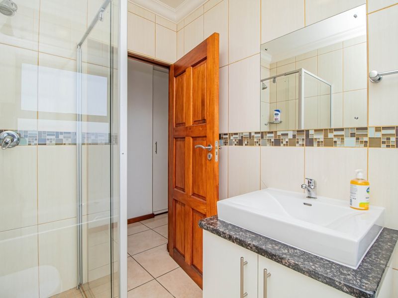 A well-maintained bathroom featuring a glass shower enclosure, vanity basin with granite countertop, and decorative mosaic tile accents.