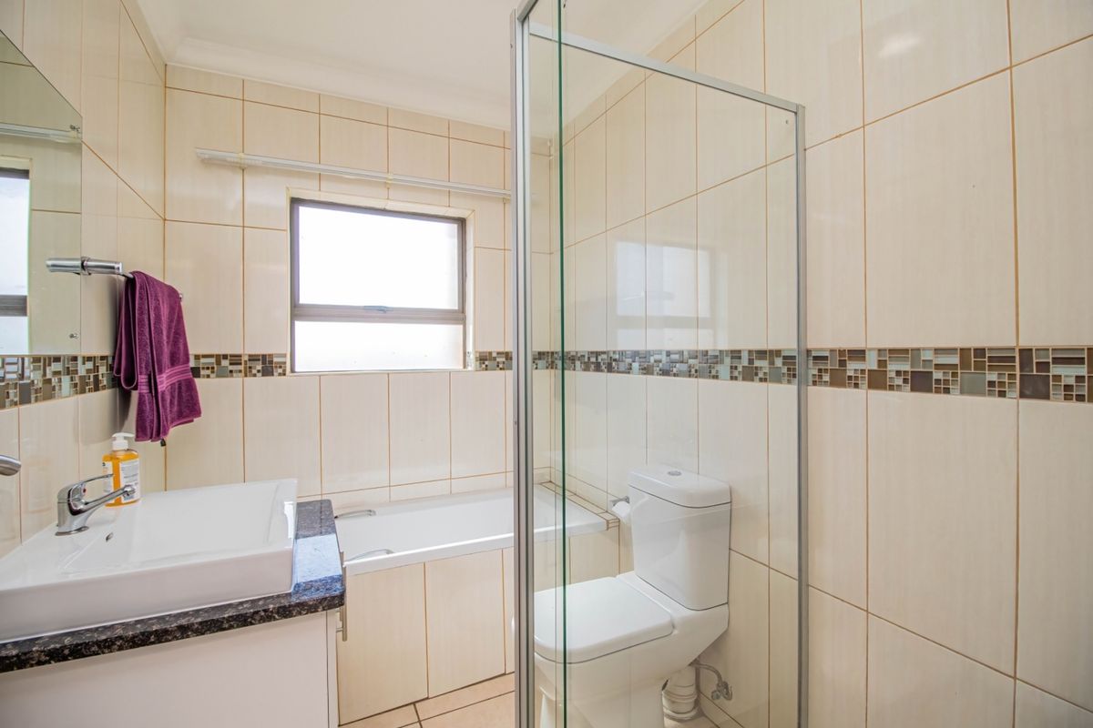 A clean, functional bathroom featuring a built-in vanity with granite countertop, a bathtub, a toilet, and a separate glass-enclosed shower with tiled walls.