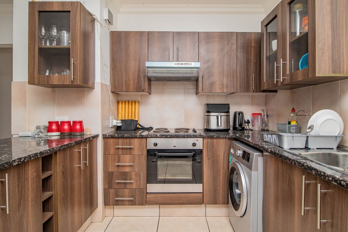 A functional kitchen featuring dark wood-look cabinetry, granite countertops, a built-in oven with hob, extractor fan, and tiled finishes throughout.