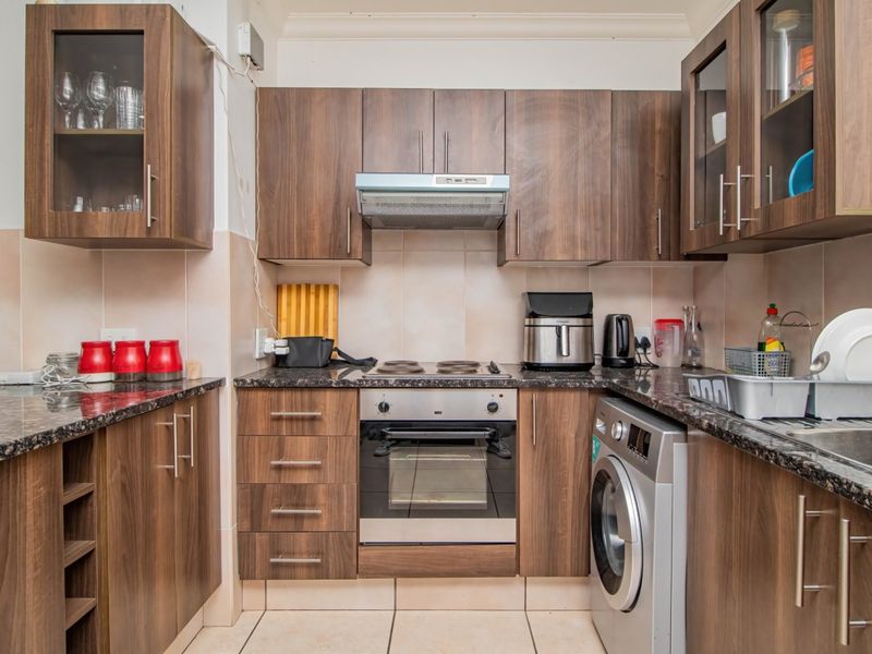 A functional kitchen featuring dark wood-look cabinetry, granite countertops, a built-in oven with hob, extractor fan, and tiled finishes throughout.