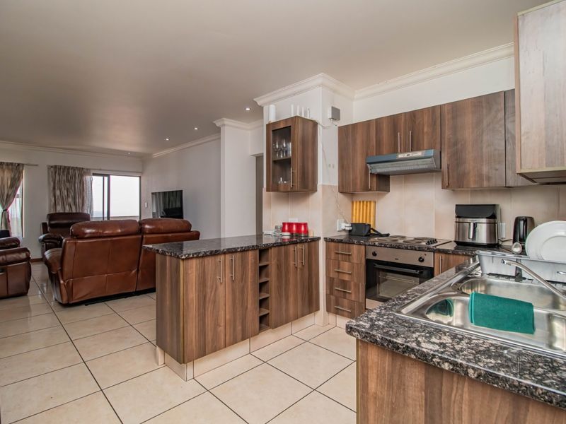 Open-plan kitchen and living area featuring wood-finish cabinetry, granite countertops, built-in appliances, and tiled flooring throughout.