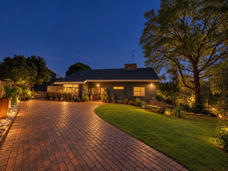 A charming front exterior view of the house at dusk, featuring a brick paved driveway, well-maintained lawn, and warm exterior lighting.