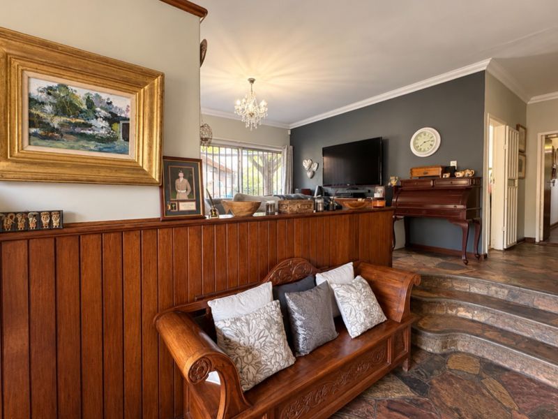 A living room featuring stone flooring, timber wall paneling, and a chandelier, with a stepped transition to an adjacent living area.