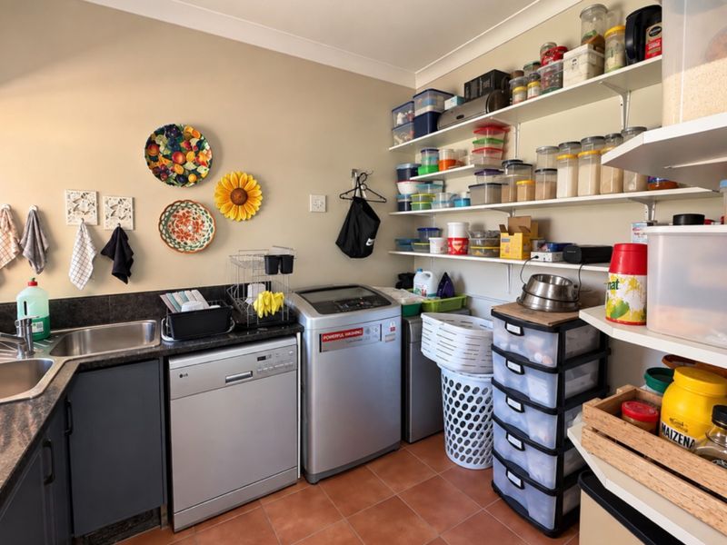A functional scullery featuring a stainless steel double sink, granite countertops, ample open shelving, and tiled flooring, providing efficient utility and storage space.