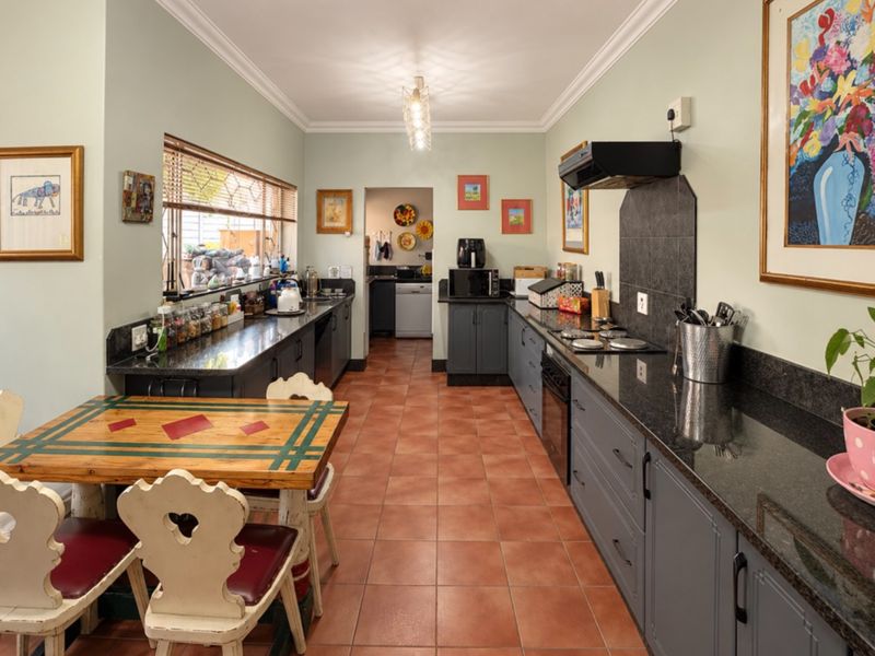 A functional kitchen featuring granite countertops, dark grey cabinetry, built-in oven and hob, and tiled flooring, with an adjacent scullery area.