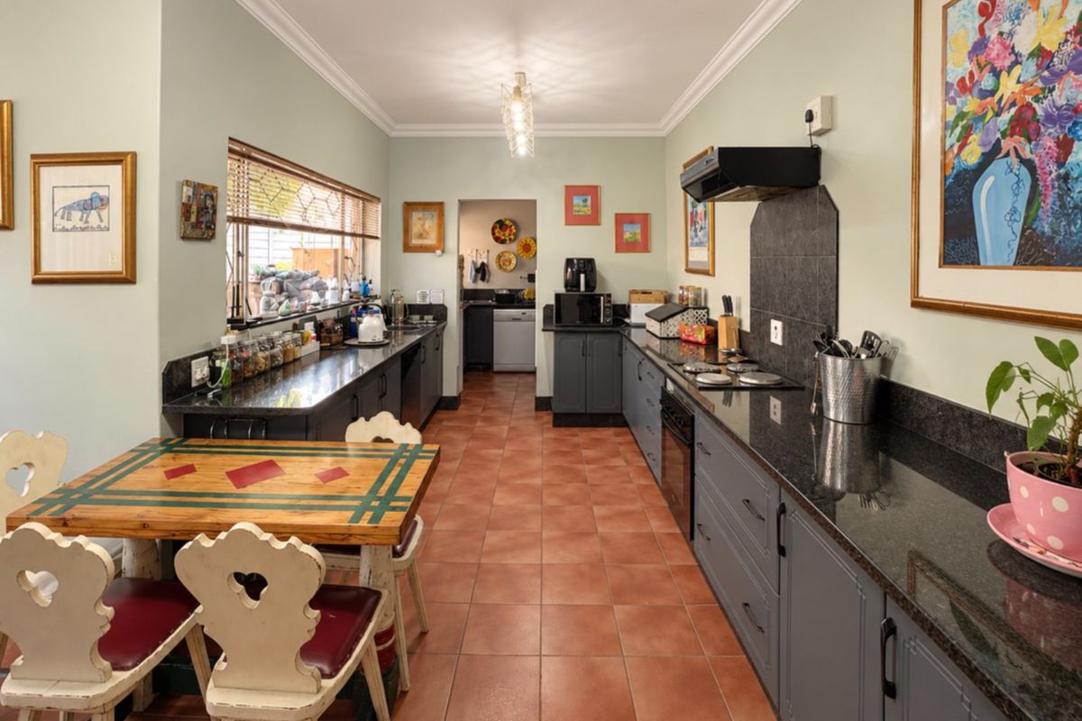 A functional kitchen featuring granite countertops, dark grey cabinetry, built-in oven and hob, and tiled flooring, with an adjacent scullery area.