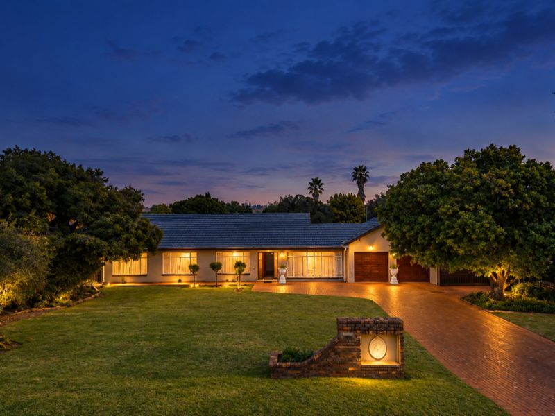 A beautifully presented single-story residence featuring a brick driveway, double garage, and well-manicured front garden, captured at dusk with warm exterior lighting.