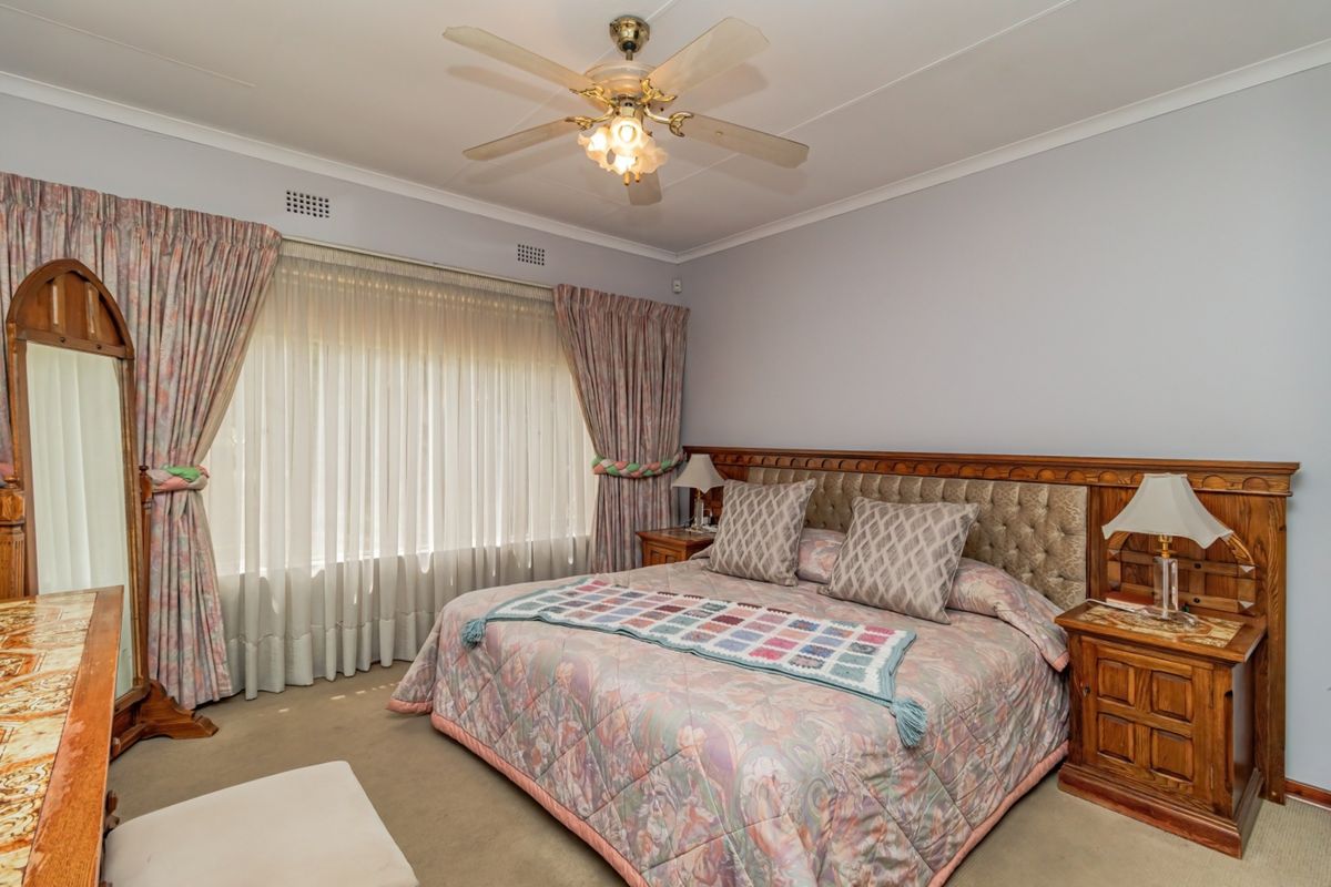 A spacious bedroom featuring a built-in wooden headboard, ceiling fan, and carpeted flooring, offering a comfortable and functional living space.