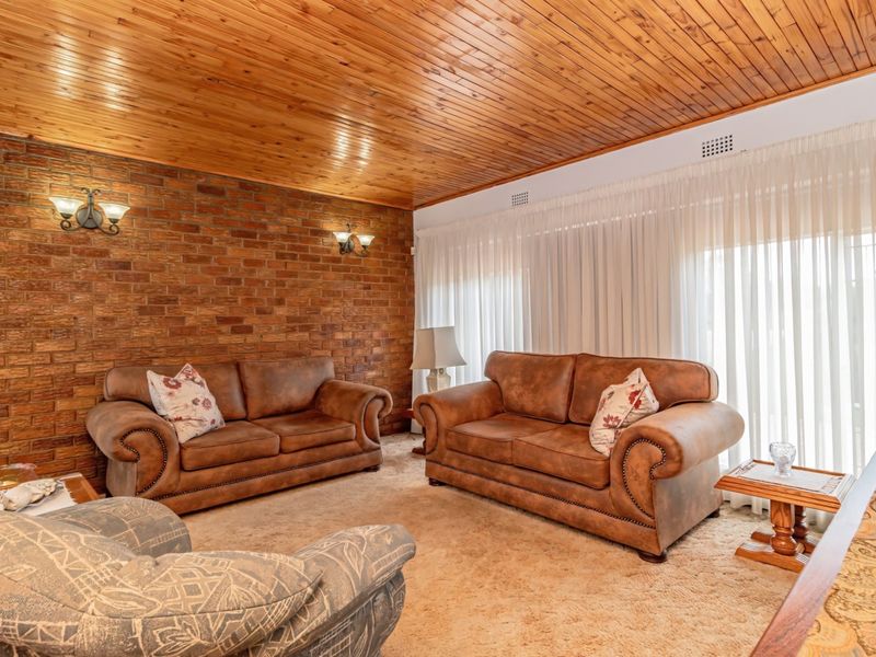 A living room featuring an exposed brick wall, timber-paneled ceiling, and carpeted flooring, offering a classic, dated aesthetic ready for modernization.