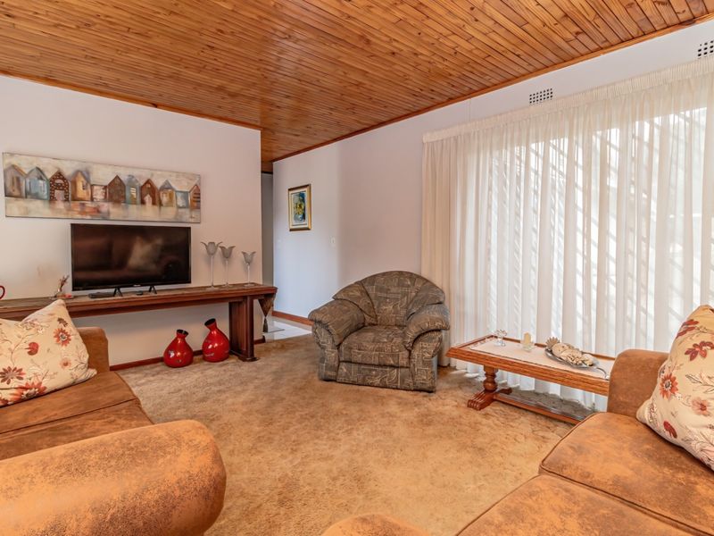A living room featuring a timber-clad ceiling, carpeted flooring, and a large sliding glass door providing access to the exterior.