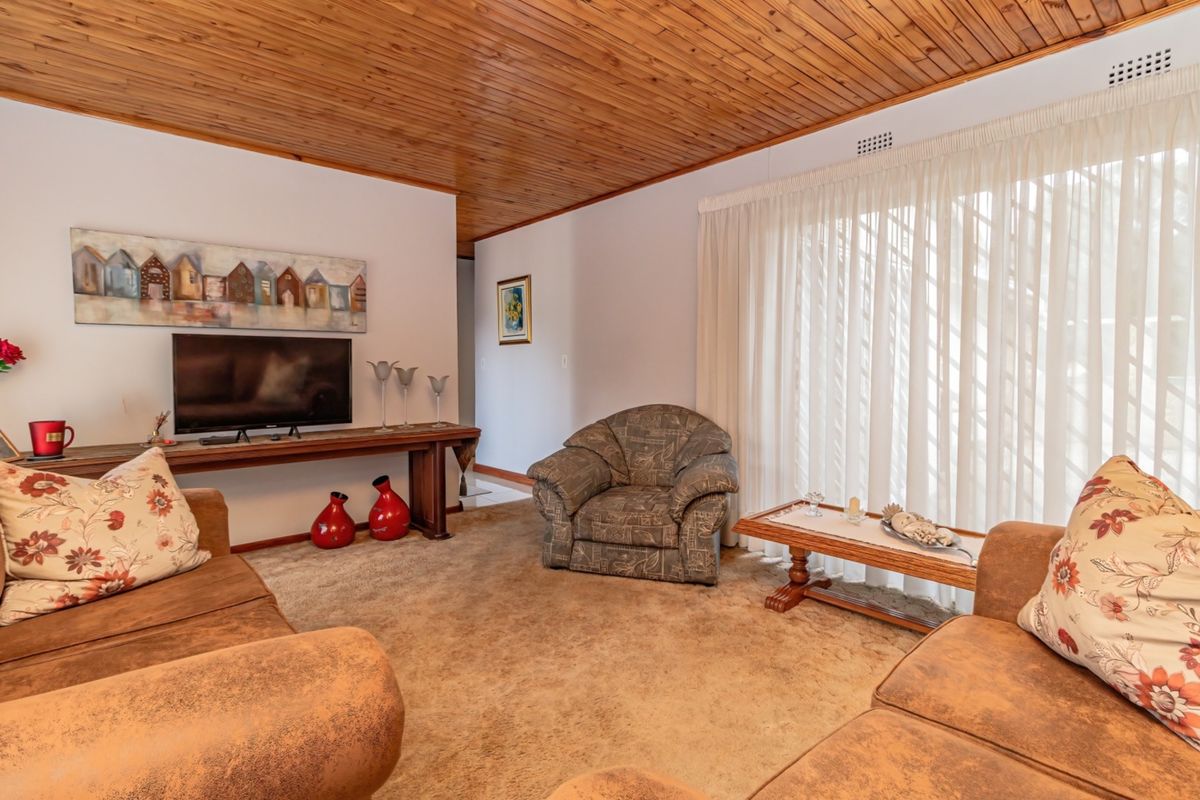 A living room featuring a timber-clad ceiling, carpeted flooring, and a large sliding glass door providing access to the exterior.