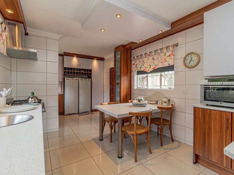 A well-maintained kitchen featuring stone countertops, built-in cabinetry, a gas hob with extractor, and integrated appliances, offering a functional and clean cooking space.