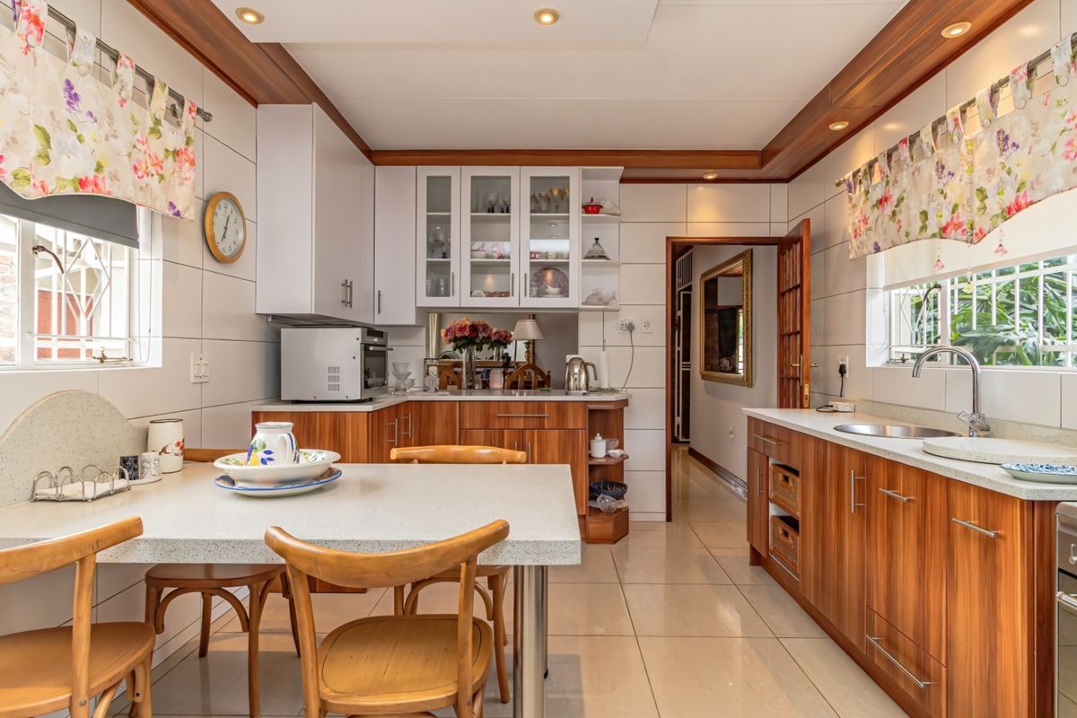A functional kitchen featuring wood-finish cabinetry, stone countertops, tiled splashbacks, and integrated lighting, offering a practical layout with an attached dining area.