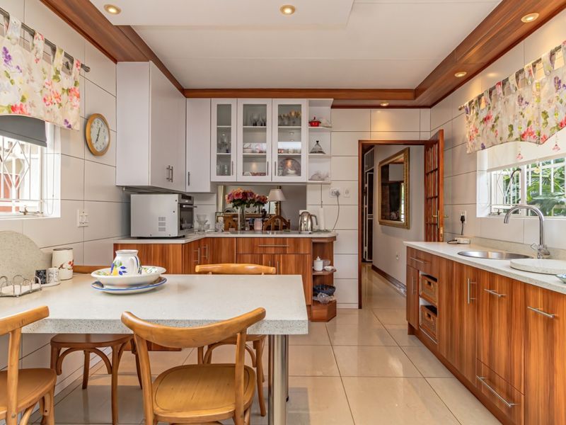 A functional kitchen featuring wood-finish cabinetry, stone countertops, tiled splashbacks, and integrated lighting, offering a practical layout with an attached dining area.