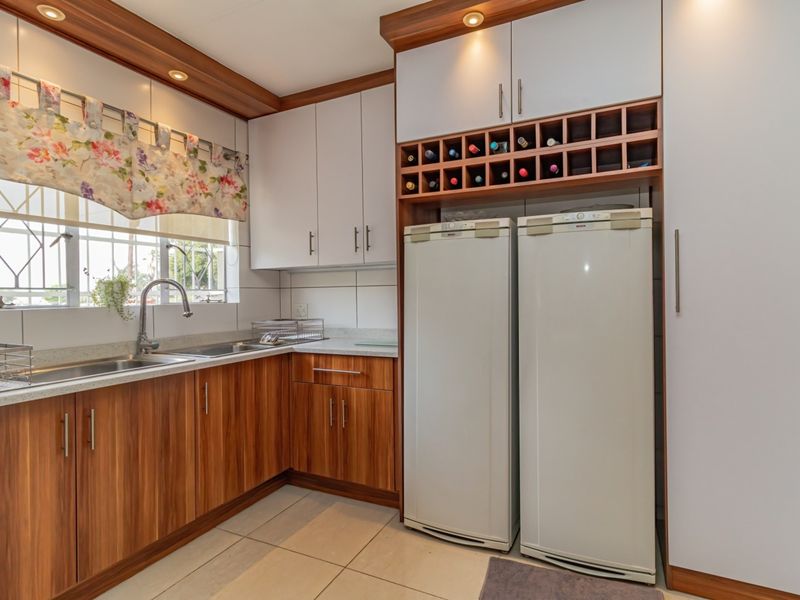 A well-maintained kitchen featuring wood-grain cabinetry, white upper cabinets, integrated wine storage, and a functional stainless steel sink area with tiled flooring.