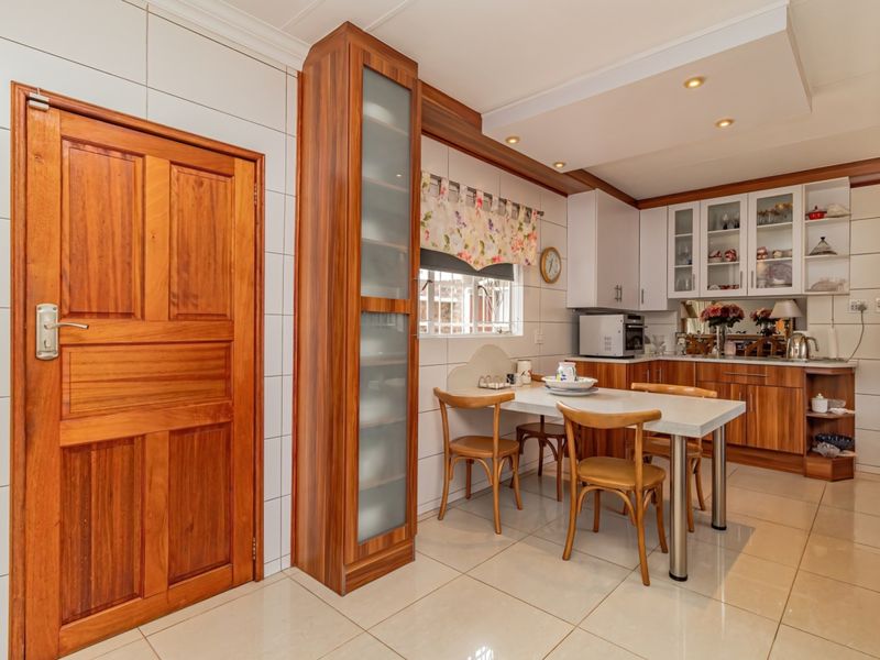 A well-maintained kitchen featuring wood-finish cabinetry, glass display units, tiled walls, and integrated lighting, offering a functional and classic culinary space.