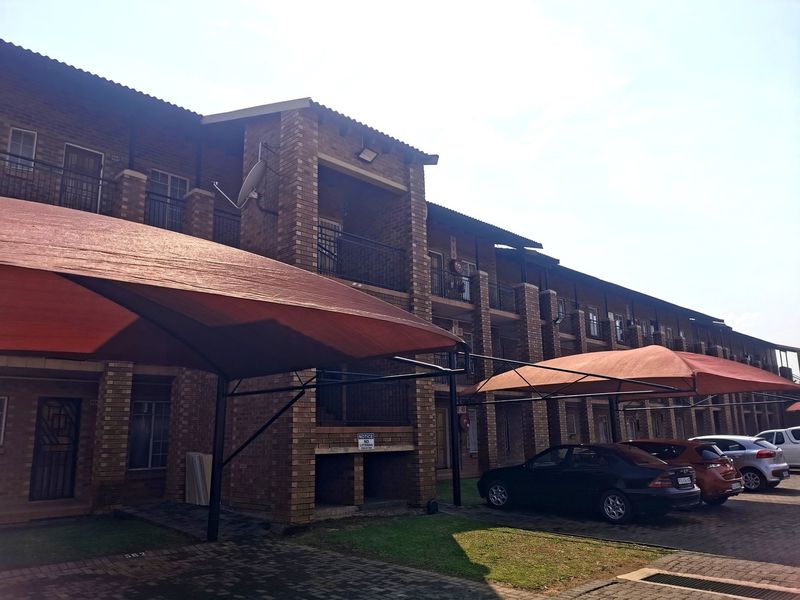 Exterior view of a multi-story apartment complex featuring face brick construction, private balconies, and dedicated shade cloth parking bays.